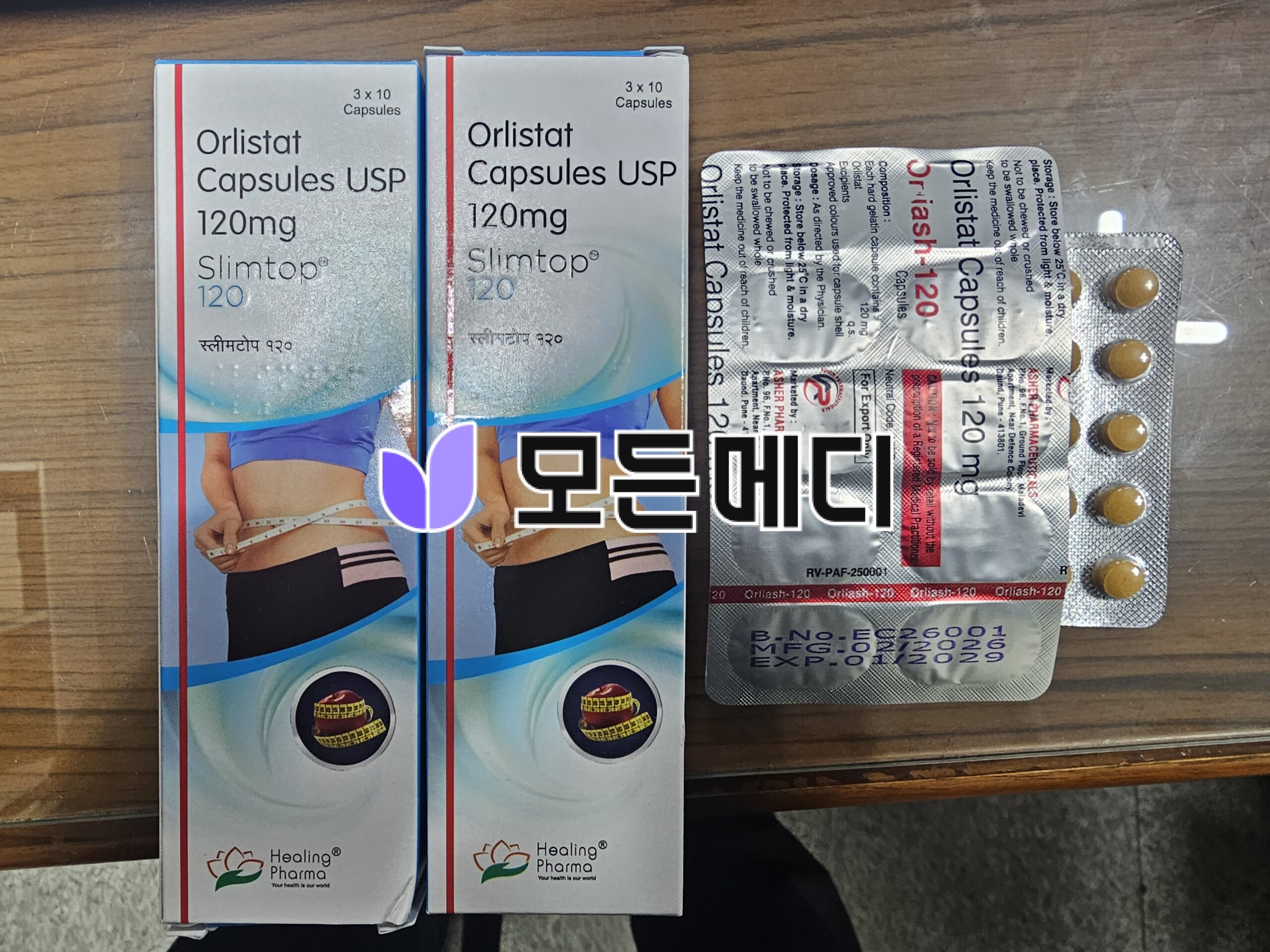 Two boxes of Orlistat 120 mg capsules (Orlistat Capsules USP) next to a blister pack of capsules on a wooden surface, Healing Pharma branding visible on the boxes and blister pack.