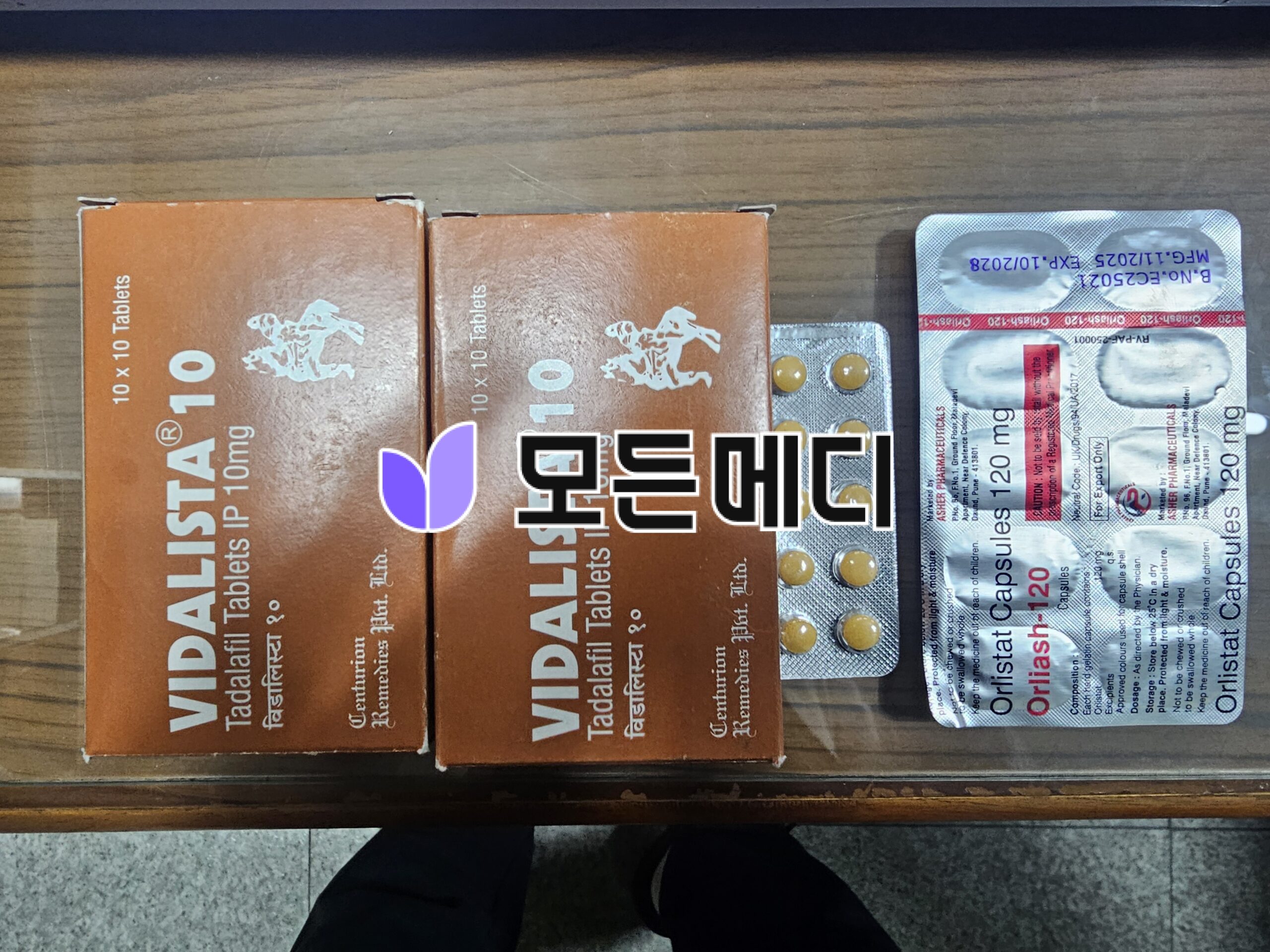 Two orange boxes labeled tablets sit on a wooden surface next to a blister pack of yellow pills.