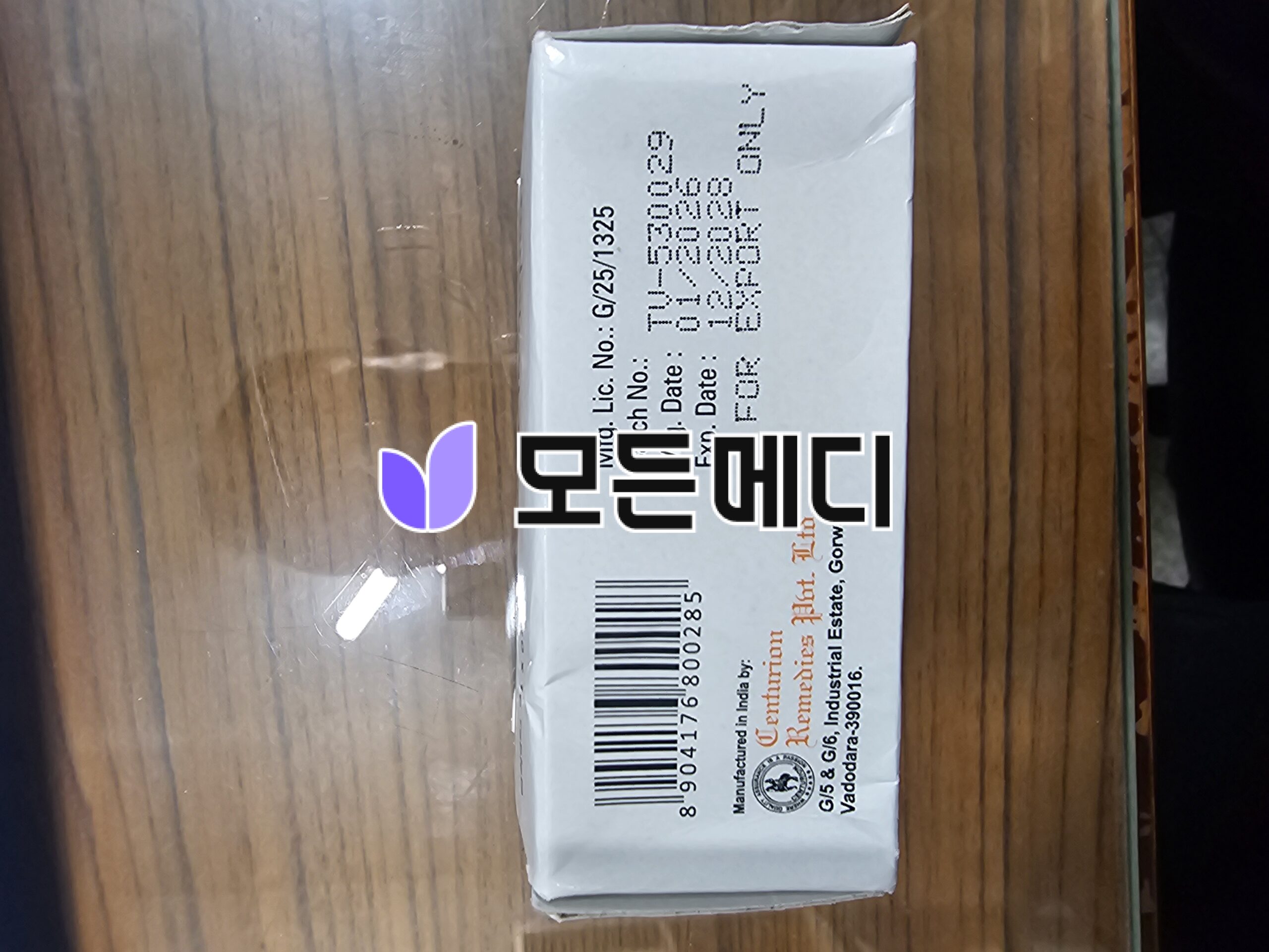 Small white cardboard parcel on a wooden surface with a barcode label and a purple logo peeking out on the side, partially rotated in the image.